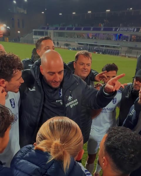 Stijn Stijnen wijst in een kring van spelers en staf van Patro Eisden op het veld na een avondwedstrijd